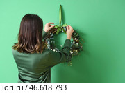 Молодая женщина вешает красивый пасхальный венок на цветную стену. Стоковое фото, фотограф Pixel_shot / Фотобанк Лори