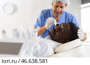 Male specialist uses ultrasonic import nozzle to care African man client face skin. Стоковое фото, фотограф Яков Филимонов / Фотобанк Лори