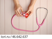 Женские руки с красным сердцем и стетоскоп на белом фоне деревянные. Кардиологическая концепция. Стоковое фото, фотограф Pixel_shot / Фотобанк Лори