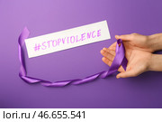 Женские руки с фиолетовой лентой и хэштегом с текстом ОСТАНОВИТЬ НАСИЛИЕ на цветном фоне. Стоковое фото, фотограф Pixel_shot / Фотобанк Лори