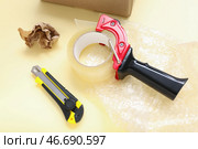 Диспенсер упаковочной ленты, нож для резки, пузырчатая пленка и мятая бумага на желтом фоне. Стоковое фото, фотограф Pixel_shot / Фотобанк Лори