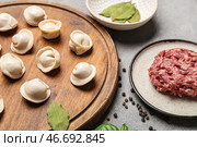 Деревянная доска с сырыми пельменями и мелко измельченным мясом на сером фоне. Стоковое фото, фотограф Pixel_shot / Фотобанк Лори