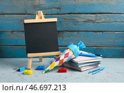 Синий школьный конус, меловая доска и канцелярские принадлежности на грубом сером столе. Стоковое фото, фотограф Pixel_shot / Фотобанк Лори