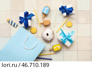Композиция для празднования Хануки с покупательной сумкой, пончиком, дрейделями и подарочными коробками на белом кафельном фоне. Стоковое фото, фотограф Pixel_shot / Фотобанк Лори