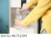 Женщина наполняет пластиковую бутылку фильтрованной водой из кулера возле синей стены. Стоковое фото, фотограф Pixel_shot / Фотобанк Лори