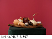 Деревянная доска с горящими свечами, тыквами, осенними листьями и сосновой шишкой на пуфике у красной стены. Стоковое фото, фотограф Pixel_shot / Фотобанк Лори