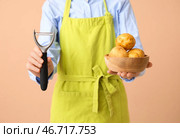 Женщина держит деревянную миску с сырыми картофелинами и овощечистку на коричневом фоне. Стоковое фото, фотограф Pixel_shot / Фотобанк Лори
