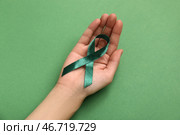 Женская рука, держащая зелёную ленту на цветном фоне. Концепция национального месяца осведомленности о церебральном параличе. Стоковое фото, фотограф Pixel_shot / Фотобанк Лори