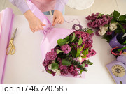 Флорист-женщина заворачивает в крафт-бумагу красивый букет сирени в цветочном магазине. Стоковое фото, фотограф Pixel_shot / Фотобанк Лори