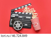 Кинохлопушка с кинолентами и попкорном на красном фоне. Стоковое фото, фотограф Pixel_shot / Фотобанк Лори