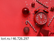 Композиция с будильником, украшениями, леденцом и конфетти на красном фоне. Концепция обратного отсчета до Рождества. Вид сверху. Стоковое фото, фотограф Pixel_shot / Фотобанк Лори