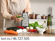 Женщина натирает цуккини на терке за столом на кухне, крупный план. Стоковое фото, фотограф Pixel_shot / Фотобанк Лори