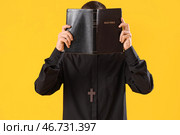 Молодой священник с Библией на жёлтом фоне. Стоковое фото, фотограф Pixel_shot / Фотобанк Лори