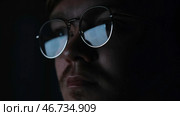 Close up of serious focused man scientist face in glasses looking at screen in the dark room. Стоковое фото, фотограф David Kashakhi / Фотобанк Лори