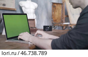 Close-up of man in black shirt sitting at the old table and typing on laptop with green chroma key screen. Стоковое фото, фотограф David Kashakhi / Фотобанк Лори