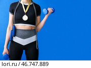 Спортивная молодая женщина с медалью за первое место, скакалкой и гантелями на синем фоне. Стоковое фото, фотограф Pixel_shot / Фотобанк Лори