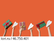 Женские руки, держащие бумажные самолетики и подарки на оранжевом фоне. Концепция новогодних каникул. Стоковое фото, фотограф Pixel_shot / Фотобанк Лори