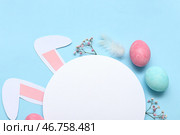 Покрашенные пасхальные яйца с пустой открыткой и бумажными заячьими ушами на синем фоне. Стоковое фото, фотограф Pixel_shot / Фотобанк Лори