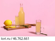Деревянная доска с бутылкой и рюмками вкусного лимончелло на розовом фоне. Стоковое фото, фотограф Pixel_shot / Фотобанк Лори