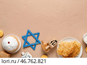 Композиция к Хануке с картофельными блинчиками, вращающимися дрейделями, пончиками и звездой Давида на бежевом столе. Стоковое фото, фотограф Pixel_shot / Фотобанк Лори