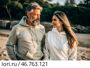 A handsome young woman and a man in white hooded sweatshirts on the beach. Template layout for hoodie design, print area layout for logo or design. Стоковое AI-изображение, AI-художник Photojuli / Фотобанк Лори