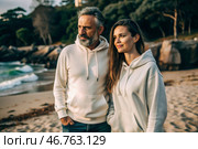 A handsome young woman and a man in white hooded sweatshirts on the beach. Template layout for hoodie design, print area layout for logo or design. Стоковое AI-изображение, AI-художник Photojuli / Фотобанк Лори