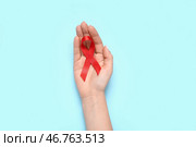 Женская рука с красной лентой на синем фоне. Концепция Всемирного дня борьбы со СПИДом. Стоковое фото, фотограф Pixel_shot / Фотобанк Лори