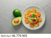 Спелый авокадо возле тарелки с вкусным гуакамоле и сухариками на текстурированном фоне. Стоковое фото, фотограф Pixel_shot / Фотобанк Лори