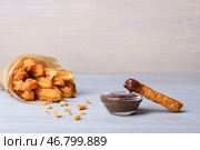 Вкусные чуррос в пергаменте и соусе из расплавленного шоколада на светлом деревянном фоне. Стоковое фото, фотограф Pixel_shot / Фотобанк Лори