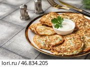 Тарелка вкусных кабачковых оладий с сметаной на сером плиточном фоне. Стоковое фото, фотограф Pixel_shot / Фотобанк Лори