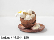 Кокосовая скорлупа с белыми шоколадными конфетами и цветком плюмерии на светлом столе. Стоковое фото, фотограф Pixel_shot / Фотобанк Лори