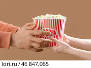Женские руки передают ведро попкорна мужским рукам на коричневом фоне. Стоковое фото, фотограф Pixel_shot / Фотобанк Лори