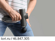 Молодой человек массирует ногу с помощью перкуссионного массажера на светлом фоне, крупный план. Стоковое фото, фотограф Pixel_shot / Фотобанк Лори