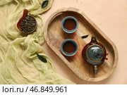 Деревянный поднос с керамическим чайником и чашками горячего заваренного чая на бежевом фоне. Стоковое фото, фотограф Pixel_shot / Фотобанк Лори