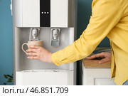Женщина наполняет чашку фильтрованной водой из кулера рядом с синей стеной. Стоковое фото, фотограф Pixel_shot / Фотобанк Лори