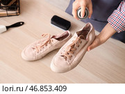 Женщина-шорник наносит водоотталкивающий спрей на пару кед на деревянном столе, крупный план. Стоковое фото, фотограф Pixel_shot / Фотобанк Лори