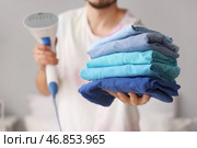 Молодой человек с парогенератором и стопкой чистой одежды дома, крупный план. Стоковое фото, фотограф Pixel_shot / Фотобанк Лори
