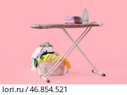 Электрический утюг с одеждой на доске и корзиной для белья на розовом фоне. Стоковое фото, фотограф Pixel_shot / Фотобанк Лори