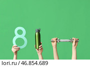 Женские руки с бумажной фигурой 8, бутылкой воды и хватом для гантели на зеленом фоне. Международный женский день. Стоковое фото, фотограф Pixel_shot / Фотобанк Лори