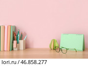 Книги, канцелярские принадлежности, перекидной календарь и очки на деревянном столе возле розовой стены. Стоковое фото, фотограф Pixel_shot / Фотобанк Лори
