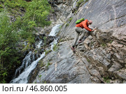 A young man in a bright orange windbreaker walks along a difficult mountain path. Via ferrata in Altai reserve. Стоковое фото, фотограф Екатерина Якименко / Фотобанк Лори