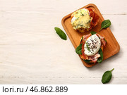 Доска с вкусными яйцами Бенедикт на белом деревянном столе. Стоковое фото, фотограф Pixel_shot / Фотобанк Лори