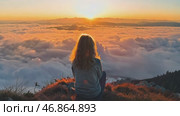 Young girl sits peacefully on top of a mountain and watches a magnificent sunset above the clouds. AI-generated item. Стоковое AI-видео, аниматор Алексей Кузнецов / Фотобанк Лори