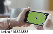 Close up of beautiful female hands holding mobile phone with chromakey on blurred room background. Стоковое фото, фотограф David Kashakhi / Фотобанк Лори