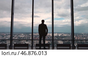 Rear view of man in formal suites who stand in front of panoramic window with city view. Стоковое фото, фотограф David Kashakhi / Фотобанк Лори