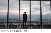 Rear view of man in formal suites who stand in front of panoramic window with city view. Стоковое фото, фотограф David Kashakhi / Фотобанк Лори