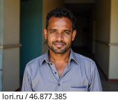 A young male resident of India stands proudly in a vibrant corridor, his warm smile reflecting joy and confidence. The colorful walls and natural light enrich the cheerful atmosphere AI. Стоковое AI-изображение, AI-художник Юлия Петровская / Фотобанк Лори