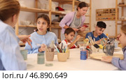 Children and teenagers sit at a table and paint ceramics at the workshop. Teacher shows how to paint a clay product after firing. Стоковое видео, видеограф Яков Филимонов / Фотобанк Лори