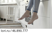 Close up for woman legs dangling with white kitchen drawers and oven on the background. Стоковое фото, фотограф David Kashakhi / Фотобанк Лори
