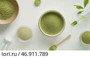Matcha powder and green tea leaves displayed on white background with measuring tools and bowls. Стоковое AI-изображение, AI-художник Сергей Толмачёв / Фотобанк Лори